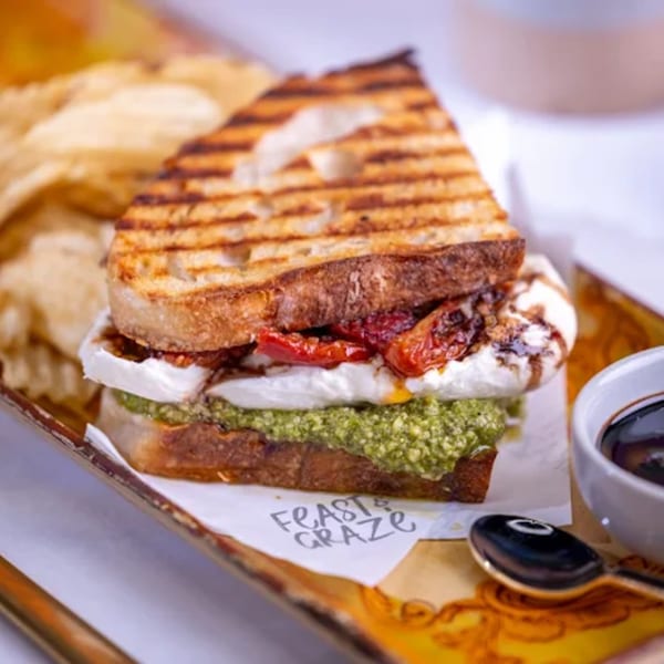 A Feast and Graze pesto and mozzarella panini with sun-dried tomatoes, chips, and balsamic glaze.