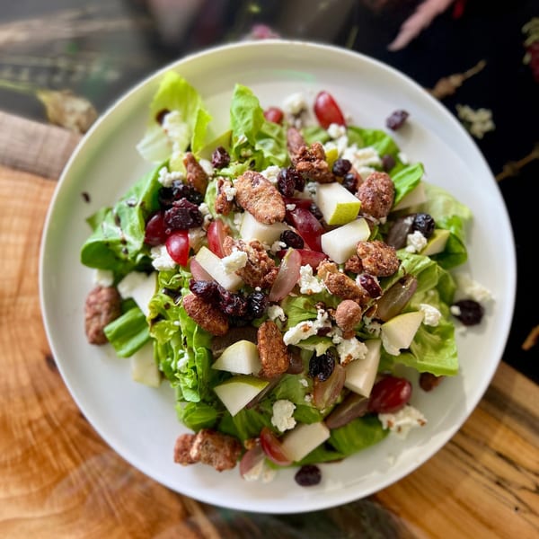 A vibrant Feast and Graze salad with greens, pears, grapes, candied pecans, and feta cheese.