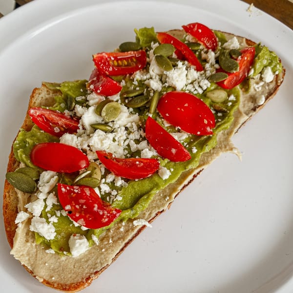 Avocado toast with cherry tomatoes, feta cheese, and pumpkin seeds on a white plate.