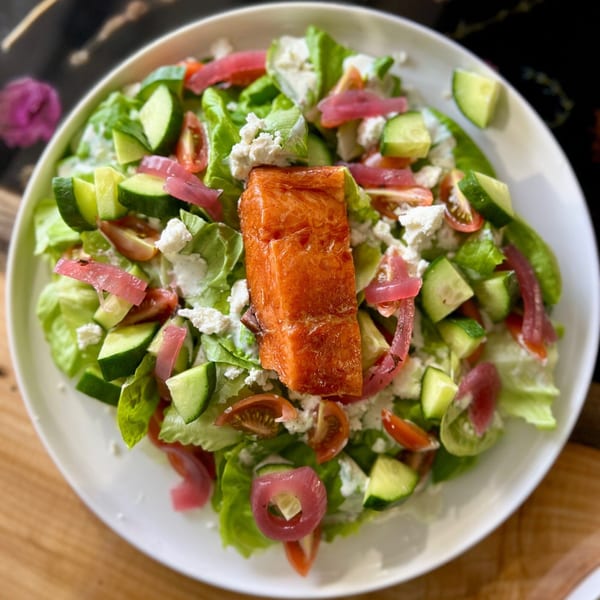 Feast and Graze's cafe salad with salmon, lettuce, cucumbers, tomatoes, pickled onions, and feta.