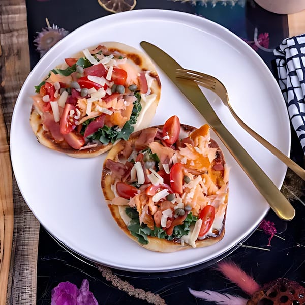 Two Feast and Graze flatbreads with salmon, tomatoes, cheese, and capers on a white plate.