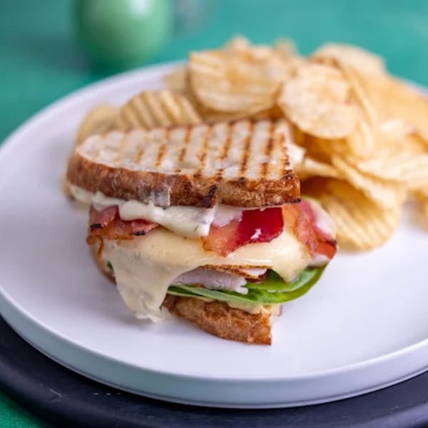 A Feast and Graze cafe panini with melted cheese, bacon, and greens, served with potato chips.